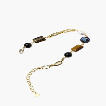 Gold chain bracelet with tiger's eye, obsidian, pearl, and iridescent abalone stones on cream background.